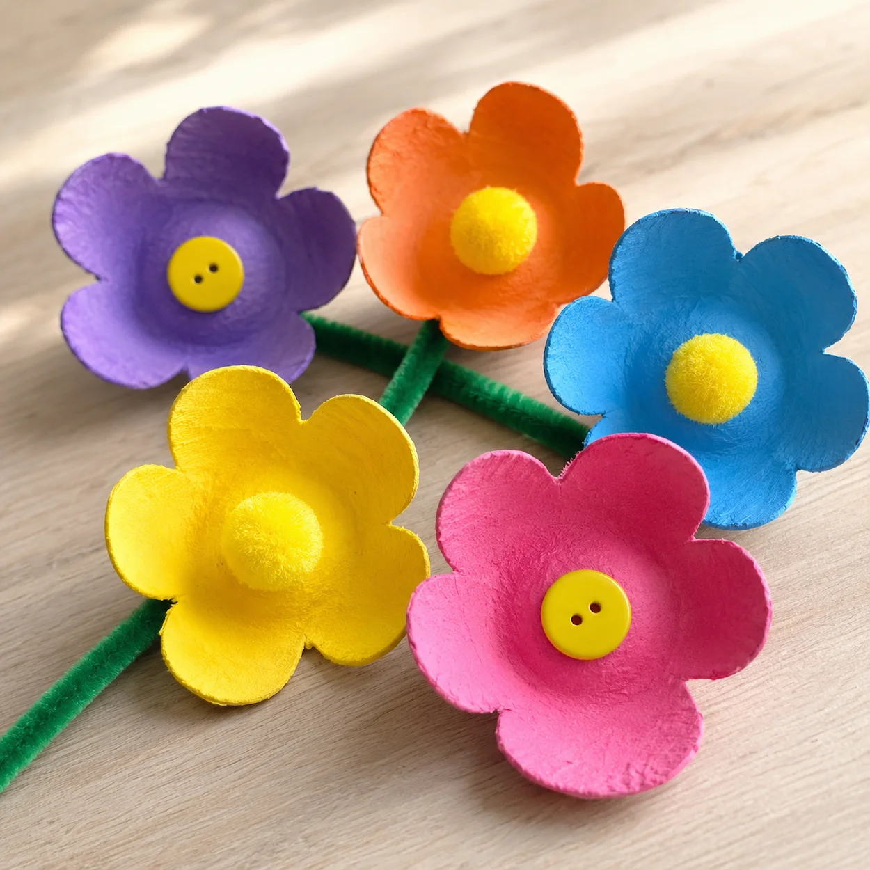 Cinq fleurs colorées fabriquées avec des alvéoles de boîtes d œufs peintes en rose jaune orange violet et bleu avec des cure-pipes verts comme tiges