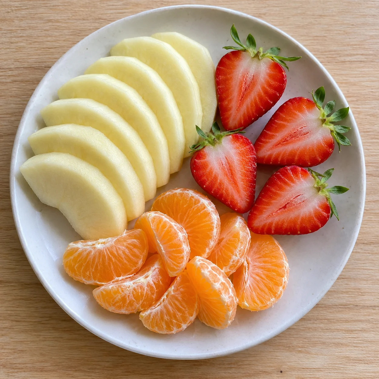 Portion idéale de fruits frais préparée pour le goûter d'un enfant : lamelles de pomme, fraises et quartiers de mandarine