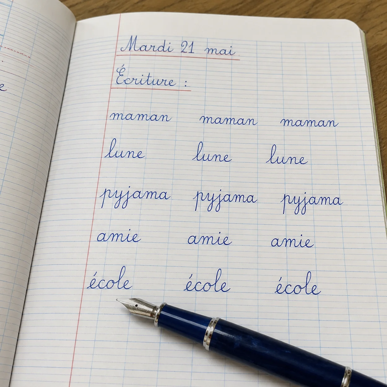Cahier Seyès ouvert montrant des mots cursifs à hauteurs variées : maman, lune, pyjama avec les lignes guides visibles