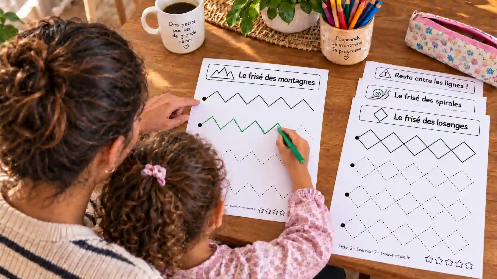 Mère guidant la main de sa fille de 4 ans sur une fiche de graphisme avec des zigzags en pointillés