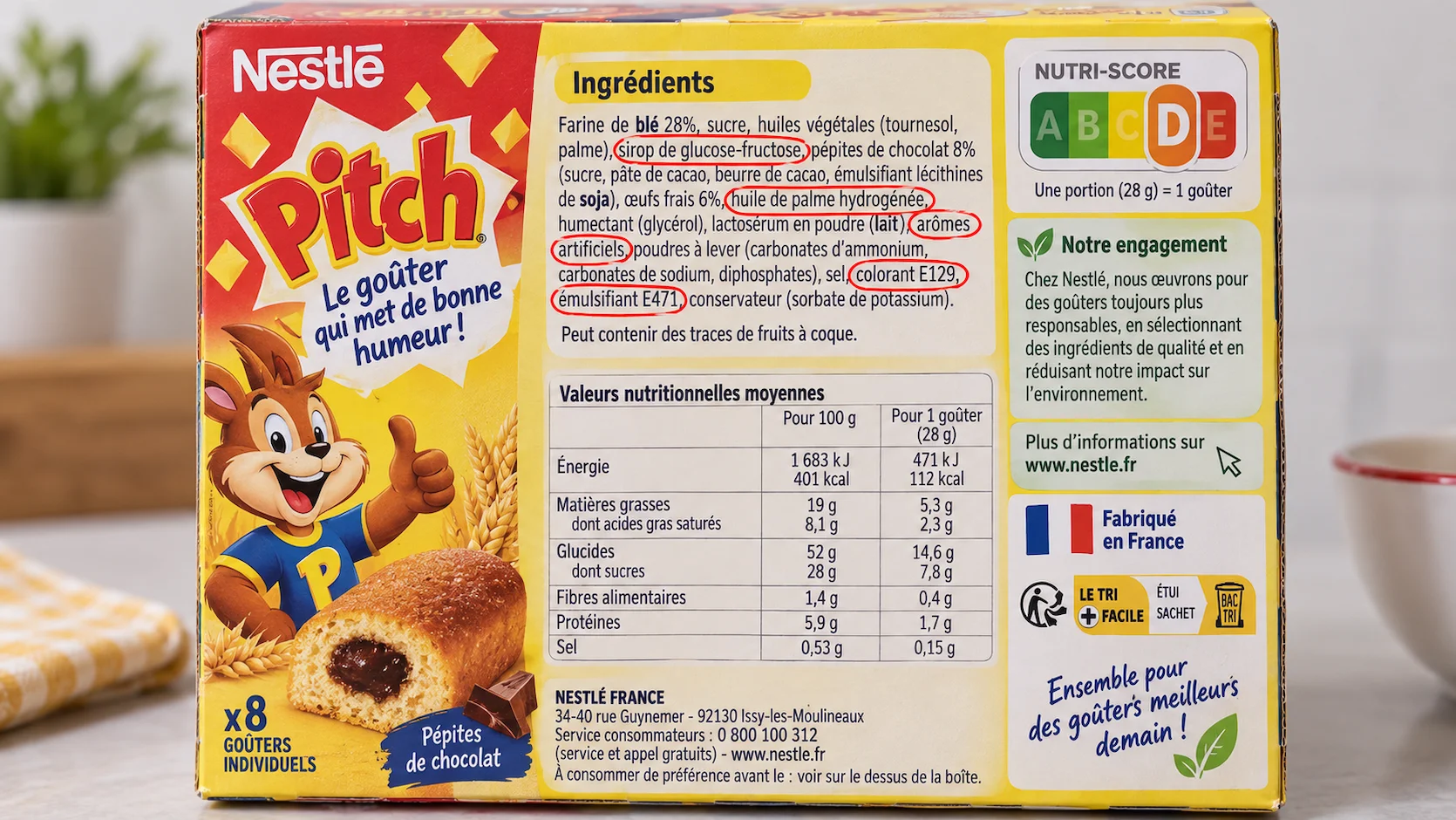 Étiquette dos d'un snack industriel pour enfants avec liste d'ingrédients montrant sirop de glucose-fructose, huile de palme hydrogénée, arômes artificiels, colorant E129 et émulsifiant E471 entourés de cercles rouges, Nutri-Score D visible